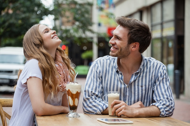 Happy couple laughing while sitting at sidewalk cafe in city