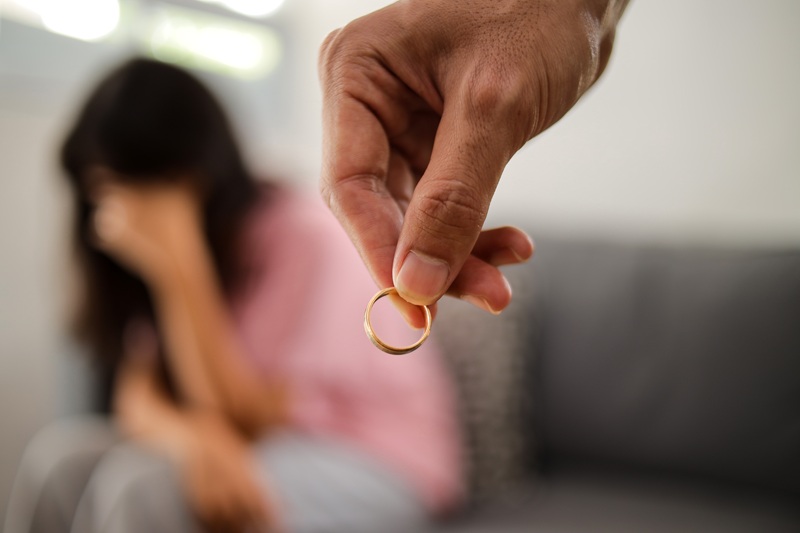 Sad couple dealing with marriage issues as man holds ring in hand, symbolizing divorce..
